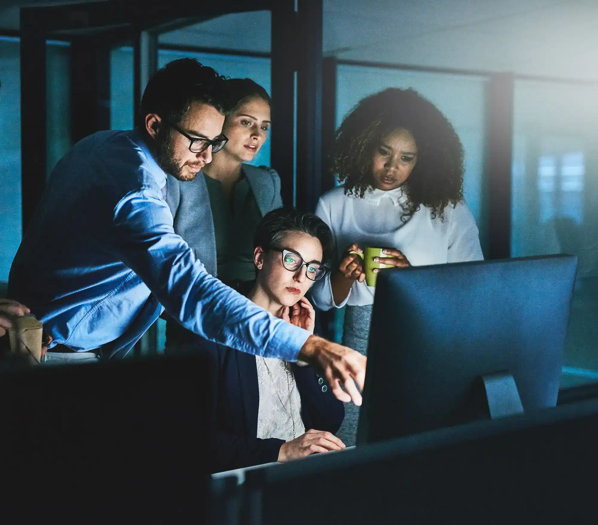 Vier Personen arbeiten gemeinsam vor einem Monitor, während ein Kollege auf den Bildschirm zeigt und das Team aufmerksam folgt.